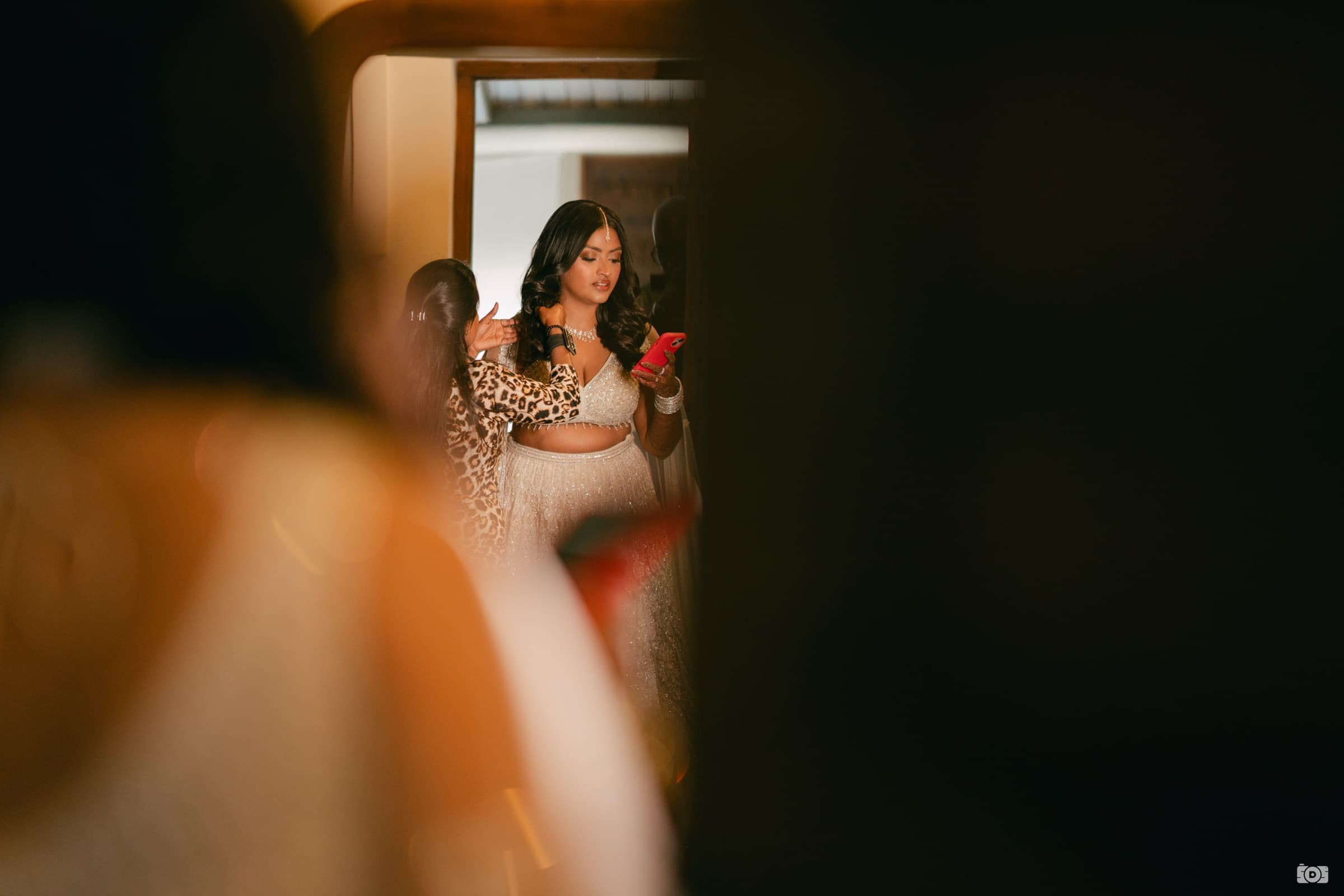 The founder, dressed for her wedding, glancing at her phone in a quiet moment while a bridesmaid adjusts her dupatta